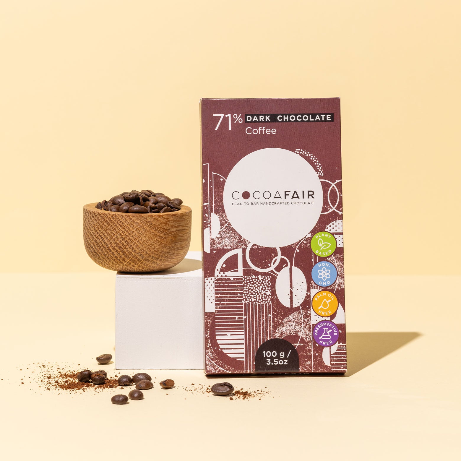 COCOAFAIR 100g 71% Dark Chocolate Lifestyle shot - Brown packaging  with coffee beans in a bowl on pastel yellow background. Coffee flavoured chocolate